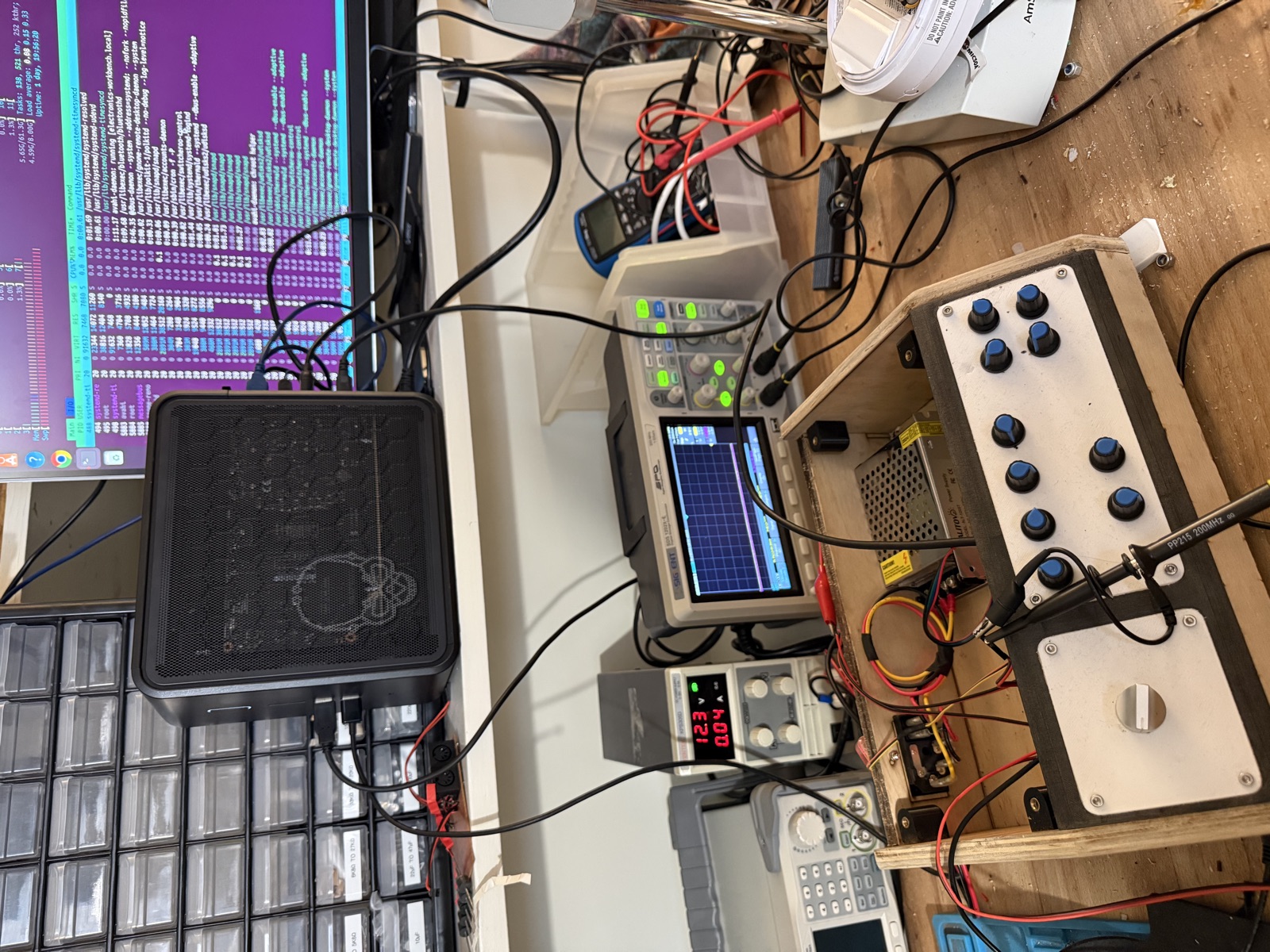 A workbench with an oscilloscope, bench power supply, debug probe, and the synth prototype with white knobs, surrounded by a tangle of cables.